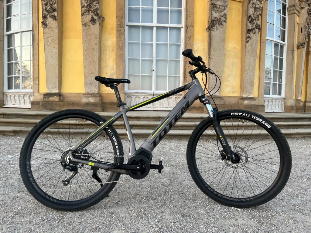 Graues E-Bike der Marke TOTEM auf der Straße vor historischem Gebäude – Beispiel für E-Bike Versicherung und sicheren Schutz deines E-Bikes.