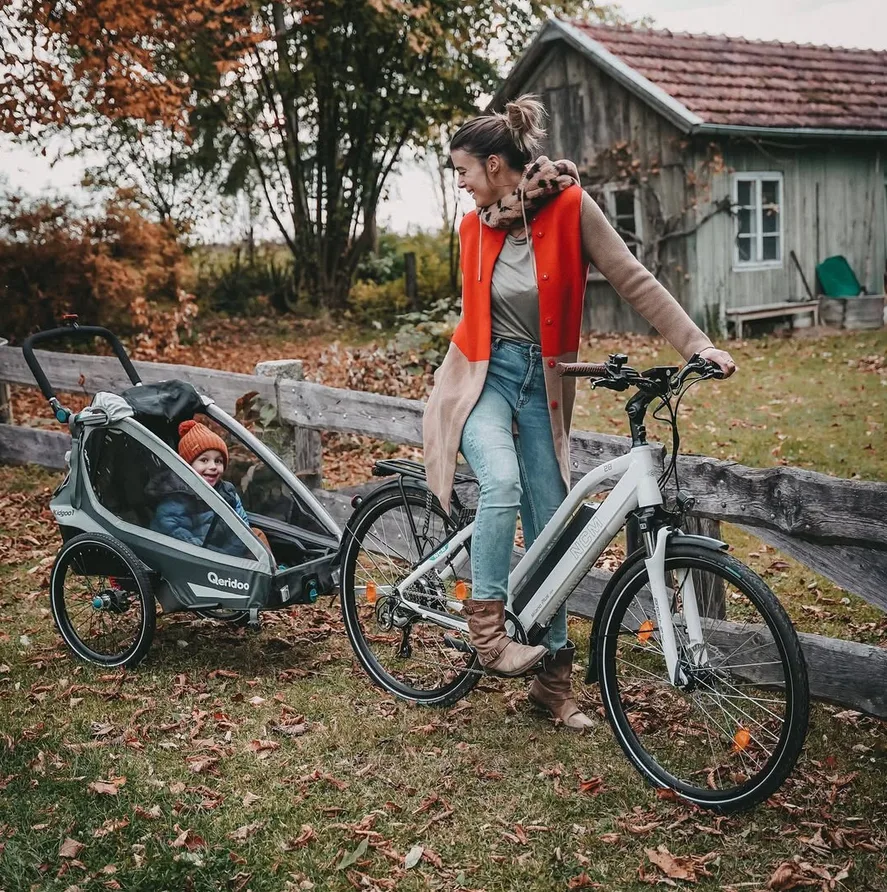E-Bike Kindersitz & Anhänger: Mutter fährt mit E-Bike, dahinter ein Anhänger mit Kind – sicher und komfortabel unterwegs.