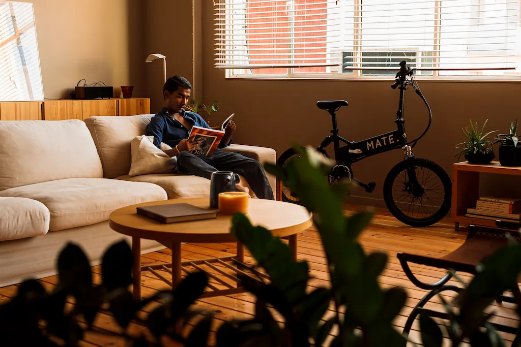 Person entspannt in einer gemütlichen Wohnung neben einem kompakten faltbaren E-Bike – Beispiel für praktisches E-Bike-Leasing für den Alltag.